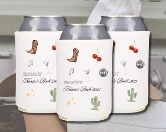 May include: Three white can coolers with a bachelorette party theme. The coolers feature a cowboy boot, musical notes, a martini glass, cherries, a cactus, and stars. The text on the coolers reads "Howdy Kenzie's Bach 2025".