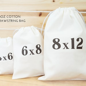 May include: Four white cotton drawstring bags with black text indicating their size: 4x6 inches, 6x8 inches, 8x12 inches.  The bags are arranged in order of size, with the smallest bag on the left and the largest bag on the right.  A clear glass bottle with a yellow label is next to the largest bag.