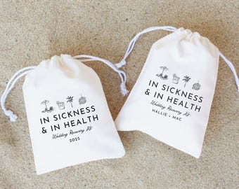 May include: Two white cotton drawstring bags with black text and illustrations. The text on the bags reads "In sickness & in health" and "Wedding Recovery Kit". One bag has the names "Hallie & Mac" and the year "2025" printed on it.