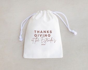 May include: White drawstring bag with the text "THANKSGIVING at the Estrada's 2026" printed in brown.