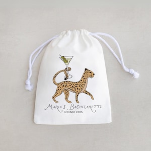 May include: White drawstring bag featuring a cartoon cheetah carrying a martini glass with olives. The bag has the text "Maria's Bachelorette Chicago 2025" in a script font. The bag is made of a soft, opaque material.