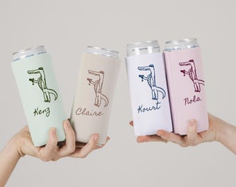May include: Four beverage can coolers in pastel colors, each with a cartoon alligator design and a name. The coolers are light green, beige, white, and pink. The alligator is holding a cocktail glass.