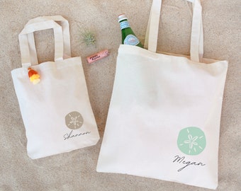 May include: Two white canvas tote bags with a sand dollar design and the names "Shannon" and "Megan" printed on them.