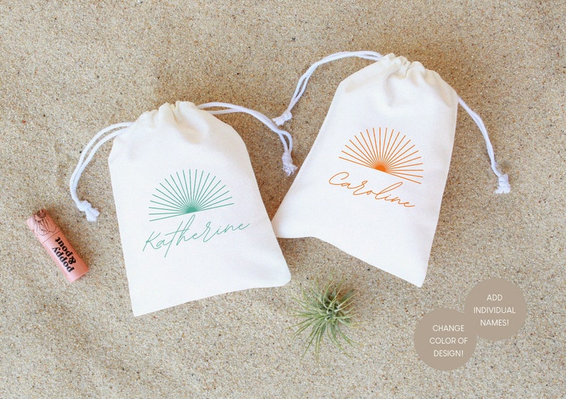 May include: Two white cotton drawstring bags with a sunburst design and personalized names. The bag on the left has a teal sunburst and the name "Katherine". The bag on the right has an orange sunburst and the name "Caroline".