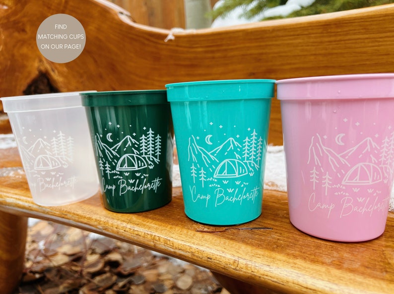 May include: Four plastic cups with a white mountain and tent design and the text "Camp Bachelorette". The cups are in the colors clear, green, teal, and pink.