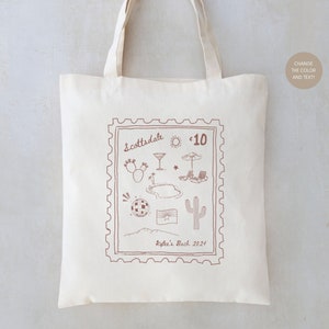 May include: A white canvas tote bag with a brown stamp design featuring the text "Scottsdale" and "$10". The stamp also includes illustrations of a cactus, a cocktail, a pool, a sun, an umbrella, and a mountain range. The text "Kylie's Bach 2024" is printed below the stamp.