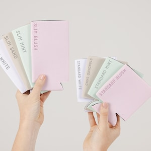May include: Two hands displaying a selection of drink koozies in pastel shades. The koozies are labelled with colour names like 'Slim Blush' and 'Standard Mint'. The koozies are in shades of pink, mint green, and beige.