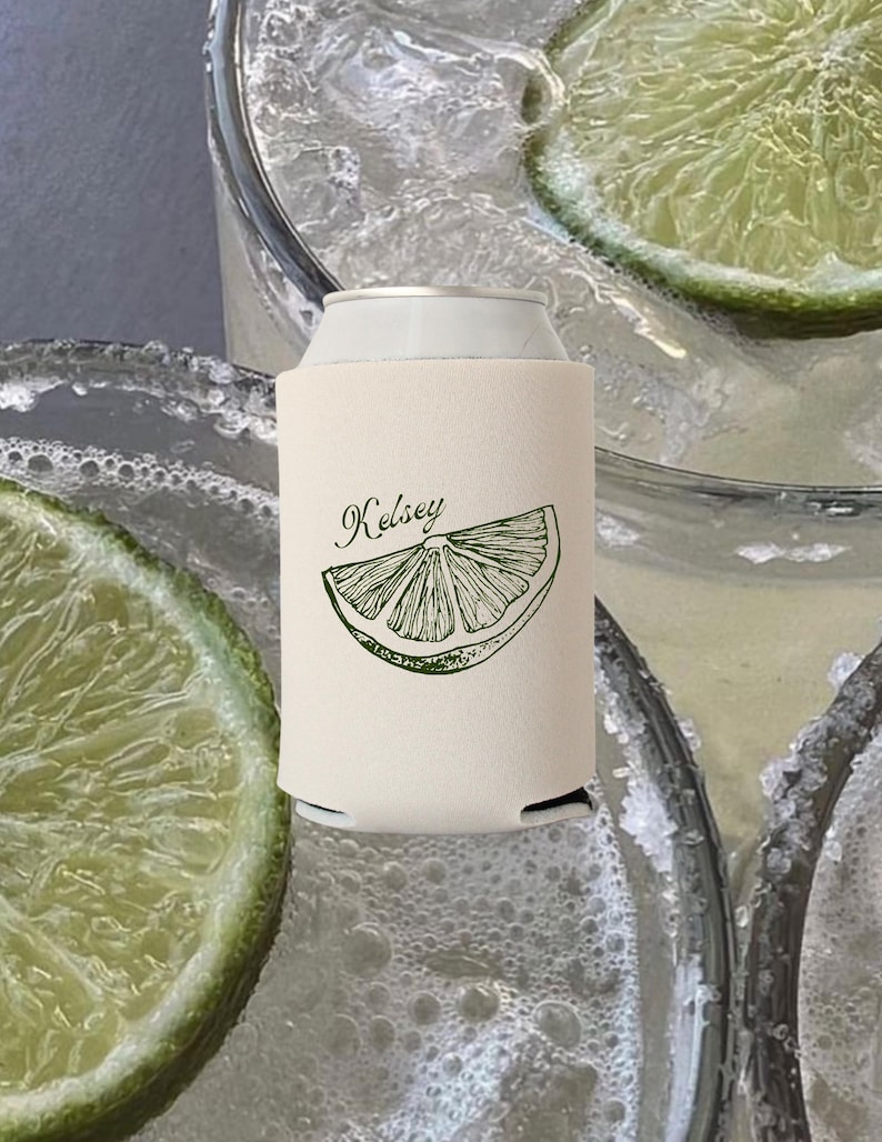 May include: A cream-colored can cooler with the name "Kelsey" and a lime slice graphic in green. The cooler is on a can, with a background of drinks with lime slices and ice.