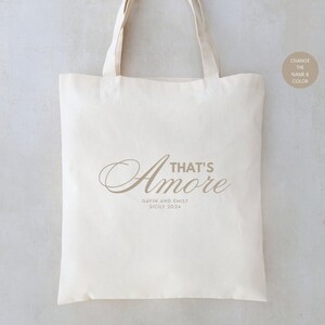 May include: A white canvas tote bag with the text "That's Amore" in a brown script font. Below the text is "Gavin and Emily Sicily 2024" in a smaller font.