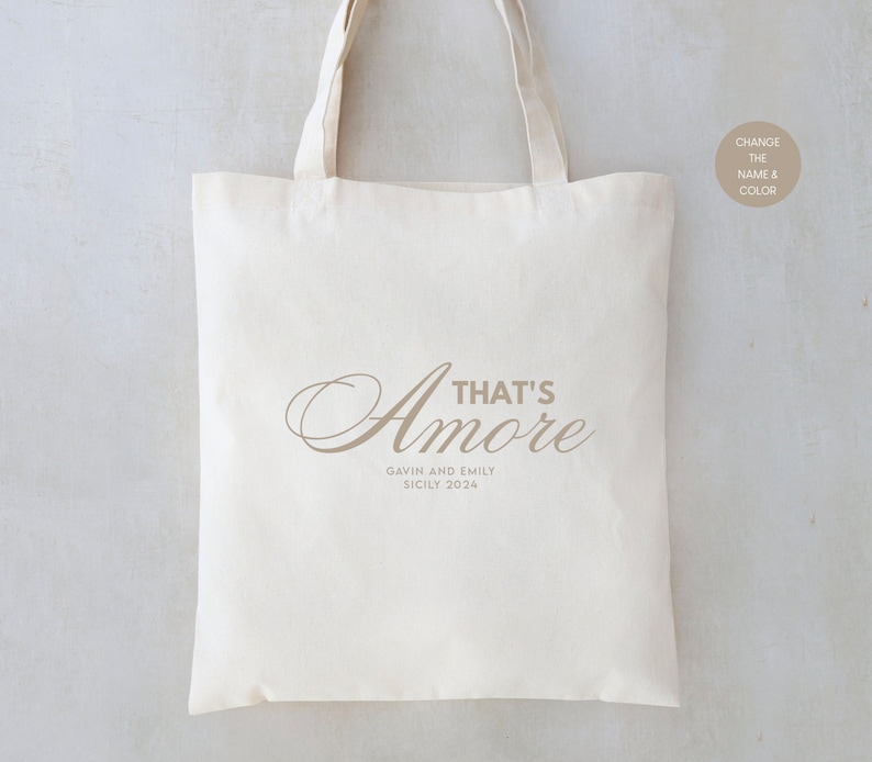 May include: A white canvas tote bag with the text "That's Amore" in a brown script font. Below the text is "Gavin and Emily Sicily 2024" in a smaller font.