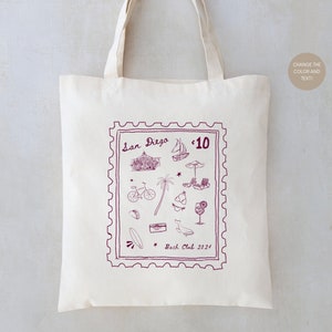 May include: A white tote bag with a purple stamp design featuring illustrations of San Diego landmarks, including the iconic carousel, a bicycle, a surfboard, and a palm tree. The stamp reads "San Diego" and "10" in the top right corner. The text "Back Club 2021" is printed below the stamp.