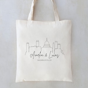 May include: White canvas tote bag with a black line drawing of the Washington DC skyline, including the Capitol Building. The text "Amelia & Lucas WASHINGTON DC" is printed below the skyline.