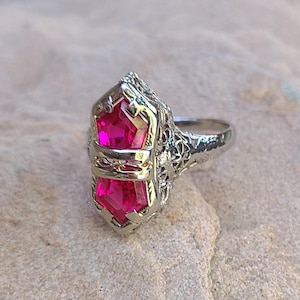 May include: A silver ring with a large, faceted, pink gemstone set in a filigree design.