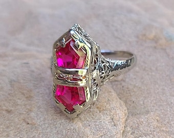 May include: A silver ring with a large, faceted, pink gemstone set in a filigree design.