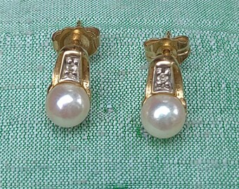 May include: A pair of gold-tone earrings with a pearl drop design. Each earring features a small, rectangular section with a cluster of small, clear stones. The earrings have a post-back closure and are set against a green background.