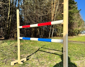 Può includere: Un ostacolo di equitazione in legno con due barre orizzontali. La barra superiore è rossa e bianca, quella inferiore è blu e bianca. I montanti hanno indicatori di altezza in cm, su un campo erboso.