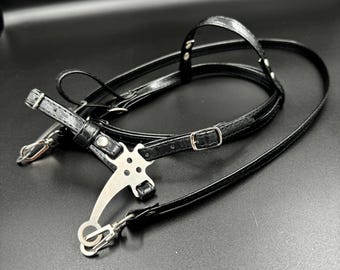 Puede incluir: Correa de cámara de cuero negro con una hebilla de metal y un gancho de metal plateado. La correa está diseñada para usarse alrededor del cuello o el hombro.