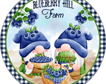May include: Two gnomes holding baskets of blueberries, one gnome is holding a jar of blueberry jam. The gnomes are wearing blue hats with blueberries on them. The background is a blue and white checkered pattern with the text "Blueberry Hill Farm" in green.