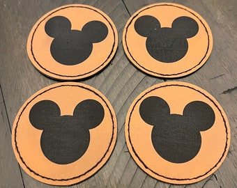 Op de afbeelding: Vier bruine leren onderzetters met een zwart Mickey Mouse silhouetontwerp.