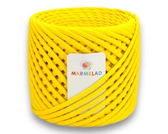 May include: A bright yellow spool of thick, woven yarn. The yarn is tightly wound, forming a cylindrical shape. A white label with the word "MARMELAD" and a rainbow heart logo is visible.