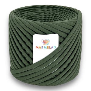 Può includere: Una grande bobina cilindrica di filato verde oliva. Il filato è avvolto strettamente, con creste visibili. Un'etichetta bianca con la scritta "MARMELAD" e un logo a forma di cuore arcobaleno è inserita al centro del filato.