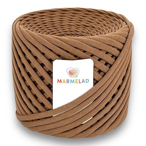 Peut inclure: Une pelote de fil de tissu marron clair, enroulée de manière serrée. Le fil est de couleur marron clair et semble être fait d'un matériau doux et texturé. Une étiquette blanche avec le mot "MARMELAD" et un logo en forme de cœur est attachée.