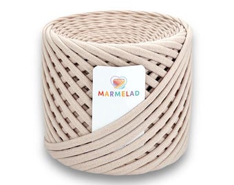May include: A cylindrical roll of beige fabric yarn, ideal for crafting. The yarn is tightly woven, with a label featuring a heart-shaped logo and the word "MARMELAD" in colorful letters. The yarn is suitable for various textile projects.