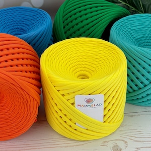 Pode incluir: Quatro novelos de fio em diferentes cores: laranja, amarelo, verde e azul. O fio é feito de um material macio e texturizado, perfeito para crochê ou tricô. O fio é etiquetado como "MARMELAD premium & yarn spain".