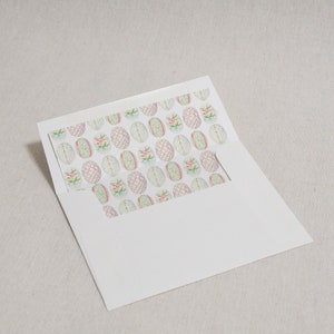 May include: A white envelope with a decorative liner featuring a repeating pattern of pastel colored eggs with floral accents.