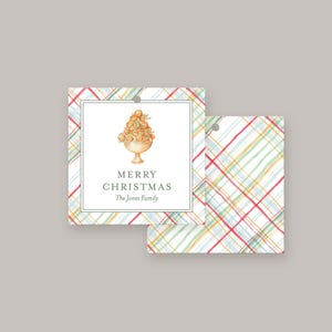 May include: A white gift tag with a red, green, yellow, and blue plaid pattern. The tag has a hole punched in the top corner. The tag has a white rectangle in the center with a watercolor illustration of a Christmas tree and the text "Merry Christmas The Jones Family".
