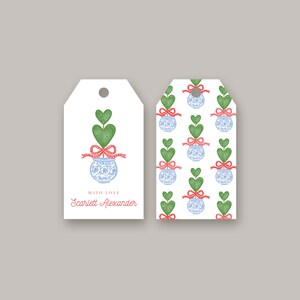 May include: White gift tags with a watercolor design. The tags feature a blue and white vase with a green heart-shaped topiary, a red bow, and the text "With Love" and a name in red. The second tag has a repeating pattern.