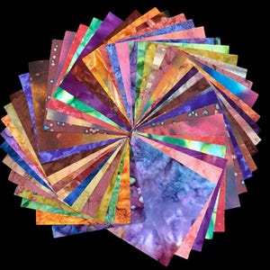 May include: A collection of square fabric swatches arranged in a circular fan pattern. Each piece features a unique batik-style dye pattern with a wide spectrum of colors including shades of blue, purple, pink, orange, yellow, green, and brown.