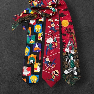 May include: Three patterned neckties featuring cartoon characters. One black tie has Looney Tunes characters. A red tie has skiers and Snoopy. The third tie is red with Bugs Bunny and a full moon.