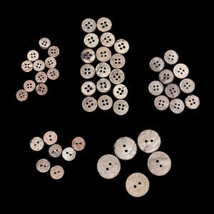 May include: A collection of natural coconut shell buttons in various sizes and shades of brown. The buttons are arranged in a pattern on a black background.
