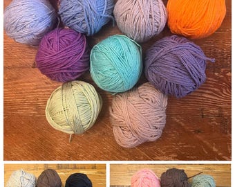 May include: A collection of colorful yarn balls in various shades, including pink, yellow, blue, purple, and orange. The yarn is arranged on a wooden surface, showcasing the texture and colors of the fiber.