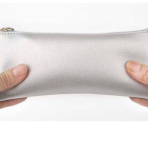 May include: A silver zippered pouch made of faux leather. The pouch is held in two hands.