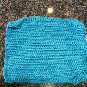 Puede incluir: Se muestra un cuadrado de ganchillo turquesa, posiblemente un paño de lavado o un paño de cocina. El artículo hecho a mano presenta un patrón de puntada apretada y texturizada y un borde doblado. El color es un verde azulado vibrante y sólido.