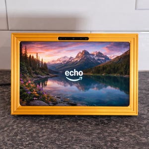 Op de afbeelding: Een geel omkaderd Echo Show-apparaat toont een schilderachtig uitzicht op een meer en bergen. Het apparaat heeft een camera en het woord "echo" met het Amazon-logo. De lijst heeft een heldergele kleur.