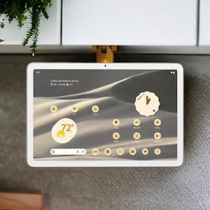 May include: A white tablet with a black screen displaying a weather app with a temperature of 72 degrees Fahrenheit and a wind speed of 11 mph. The tablet is mounted to a white cabinet with a gold bracket.