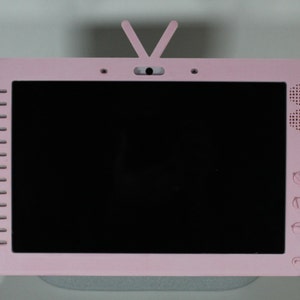 Peut inclure: Une télévision rose avec un écran noir et une petite antenne sur le dessus. La télévision a un haut-parleur sur le côté droit et des boutons sur le côté droit.