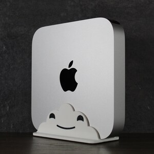 May include: A white Apple computer with a black Apple logo on the front. The computer is sitting on a white stand with a cloud design.