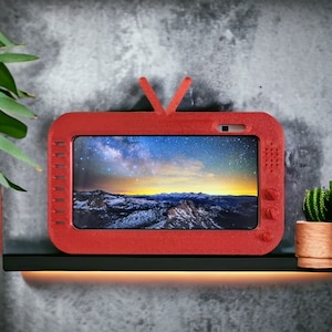 May include: A red, plastic, retro-style television with a screen displaying a night sky with stars. The television has a small camera lens on the top.