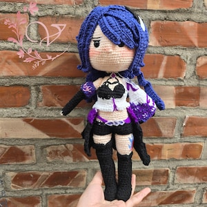 May include: Crocheted doll with blue hair, wearing a black and white outfit with purple accents. The doll is holding a sword and has a determined expression.