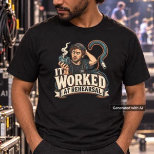 May include: A black t-shirt featuring a graphic of a confused audio technician holding a smoking DI box. The design includes a coiled XLR cable and the text "IT WORKED AT REHEARSAL" in bold, stylized lettering across the center of the chest.