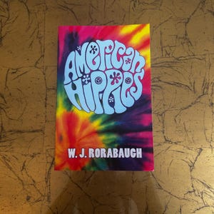 May include: A book cover with the title "American Hippies" in light blue, stylized lettering. The background is a vibrant tie-dye pattern in shades of red, pink, yellow, and purple. The author's name, W.J. Rorabaugh, is printed at the bottom.
