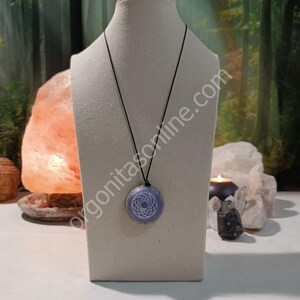 Peut inclure: Un collier avec un pendentif chakra violet et blanc sur un cordon noir. Le pendentif est rond et présente un motif de mandala blanc. Le collier est présenté sur un mannequin blanc.