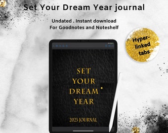 Peut inclure: Une tablette numérique noire avec un texte doré superposé qui indique "Set Your Dream Year 2023 Journal". La tablette est sur un fond blanc avec des paillettes dorées.