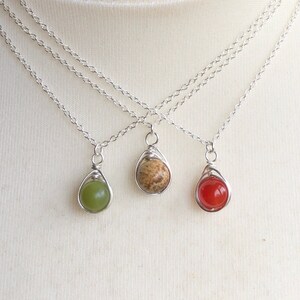 May include: Three silver chain necklaces with different colored gemstone pendants. The pendants are green, brown, and red.