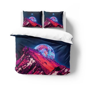 Puede incluir: Una funda nórdica con fondo azul oscuro que presenta un planeta rosa y azul elevándose sobre una cordillera. El planeta está rodeado de estrellas y la cordillera es de un rosa y morado vibrantes.