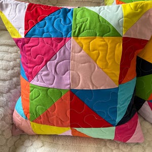 May include: Two vibrant throw cushions with a patchwork design. The cushions display a range of bright colours, including red, pink, yellow, green, and blue. Each cushion is approximately 45 cm square and has a quilted pattern.